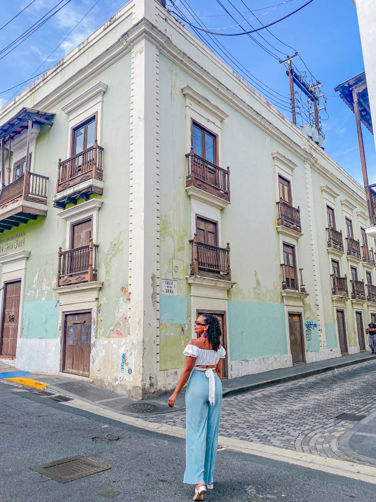 Foto da Camilli de costas usando calca azul e top branco na cidade antiga de San Juan no post roteiro de 3 dias em Porto Rico