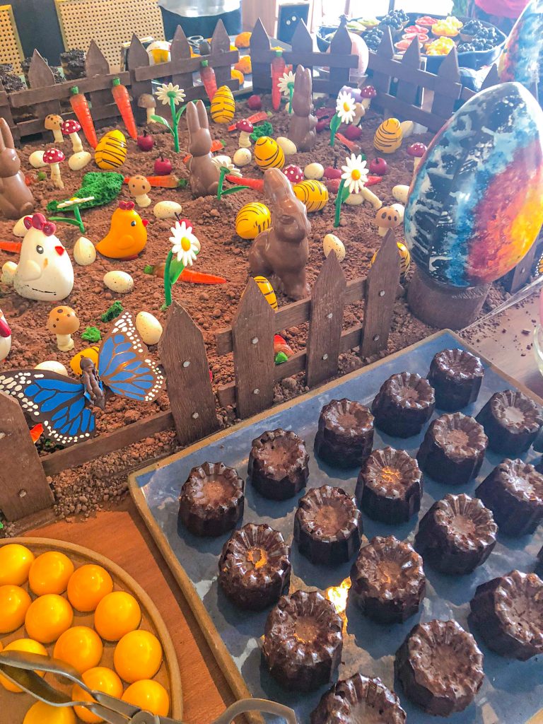 Foto de uma mesa decorada para a Páscoa, com ovos de chocolate, bolode chocolate, coelhos de chocolate e decoração de jardim com flores e galinhas no Brunch do Copacabana Palace