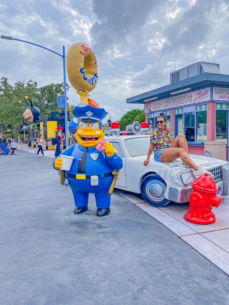Foto da Camilli sentada num carro fictício olhando para um policial em estátua no parque da Universal