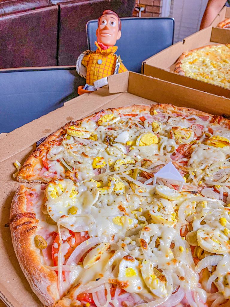 Foto de uma pizza portuguesa e do boneco Woody em Orlando