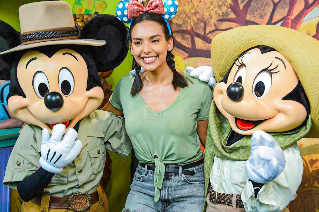 Foto da Camilli com camiseta verde, 2 tranças no cabelo e orelhinha da Minnie entre os personagens da Disney Mickey e Minnie no post sobre Disney e Universal na pandemia