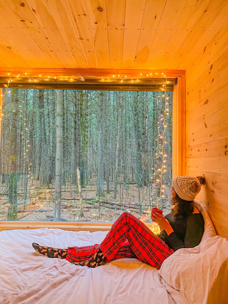 Foto da Camilli com pijama de natal e touca, sentada na cama olhando lora janela na cabine em Catskills
