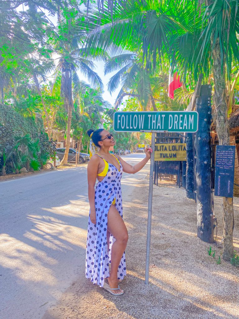 Foto da Camilli com vestido de bolinha em frente a placa Follo chata dream lugares instagramaveis de Tulum