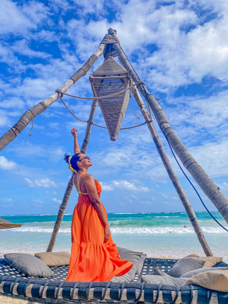 Foto da Camilli com vestido laranja em pé em frente a praia, no hotel nômade para o post  lugares instagramaveis de Tulum